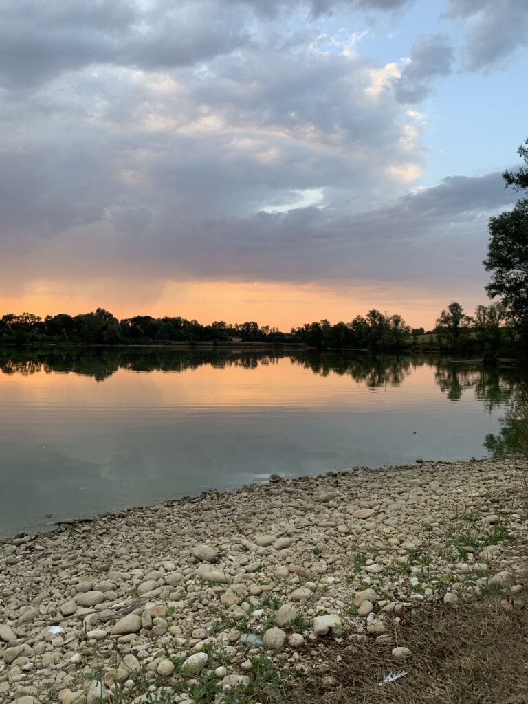 Bord du plan d'eau des Écuries d'Eurofarm à Confrançon avec un paysage naturel au coucher du soleil.